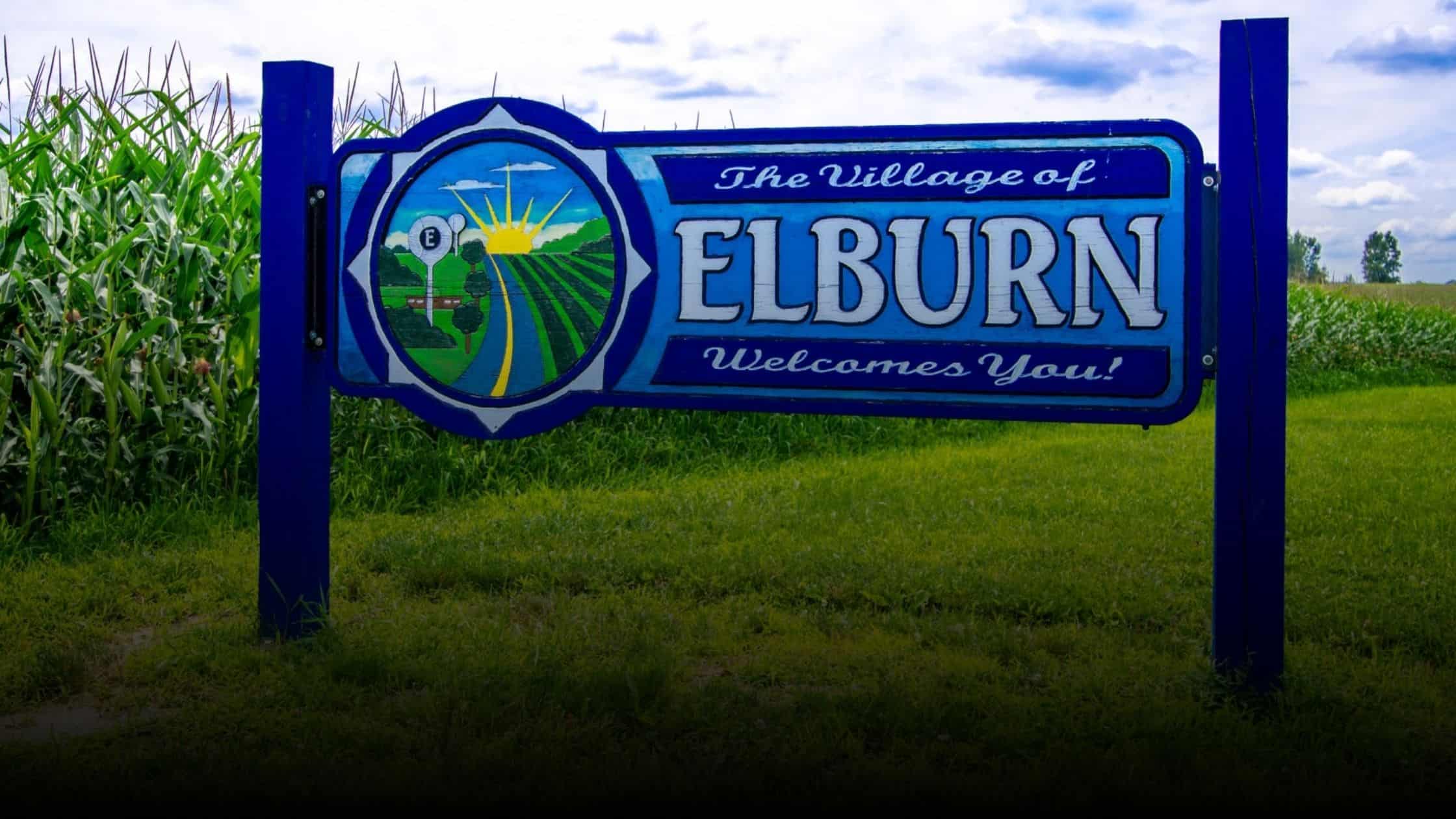 A vibrant welcome sign for the Village of Elburn, Illinois, set against a backdrop of lush green cornfields.